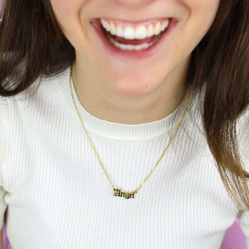 Model wearing Gold plated stainless steel necklace with the word 'angel' written in a gothic font