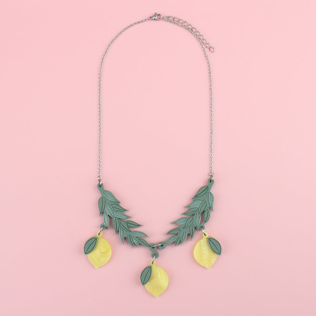 Yellow acrylic lemons hanging from matt sage green branches on a stainless steel chain