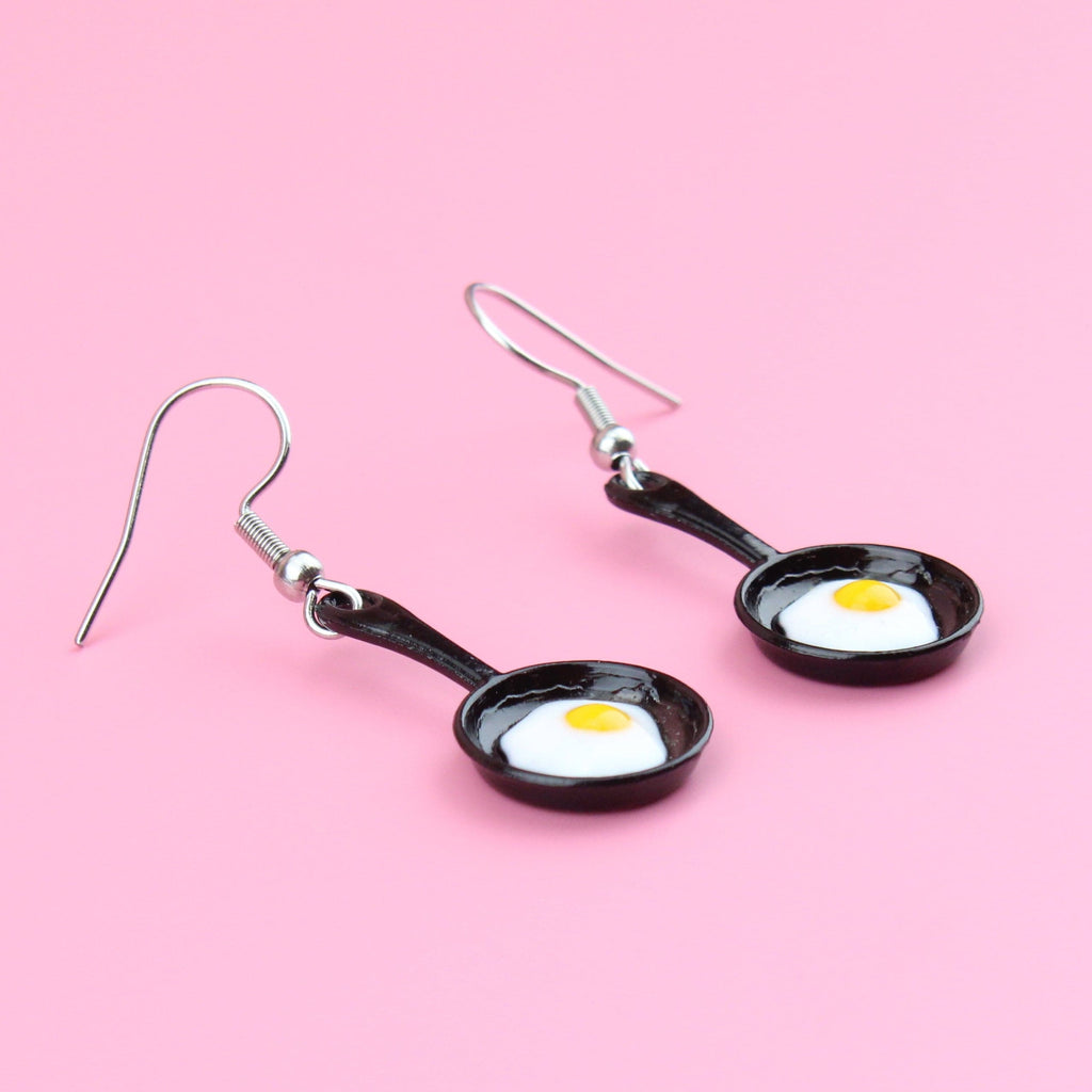 Charms that feature a fried egg in a frying pan on stainless steel earwires