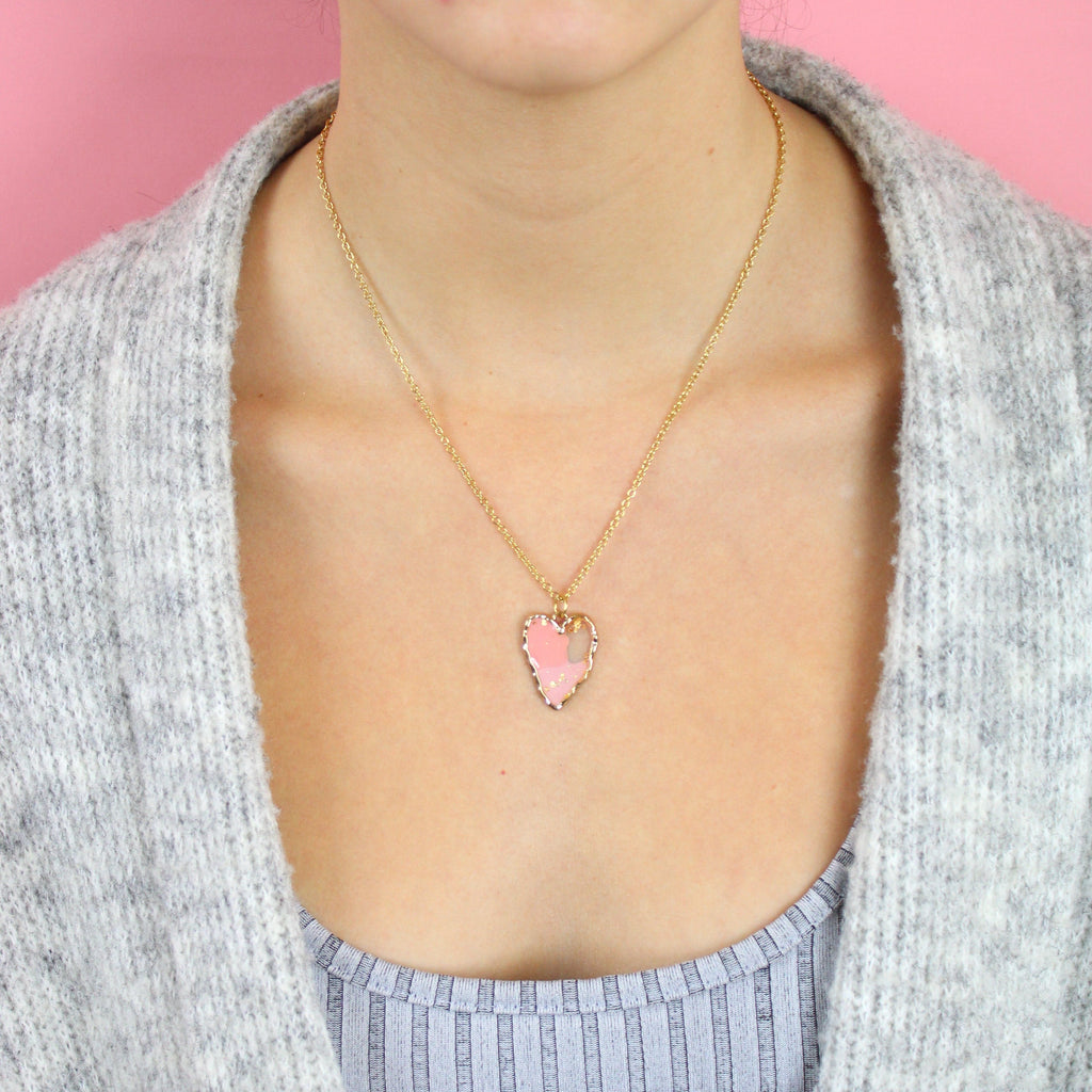 Model wearing gold plated stainless steel necklace with a gold heart pendant featuring 2 shades of pink in the middle and gold speck